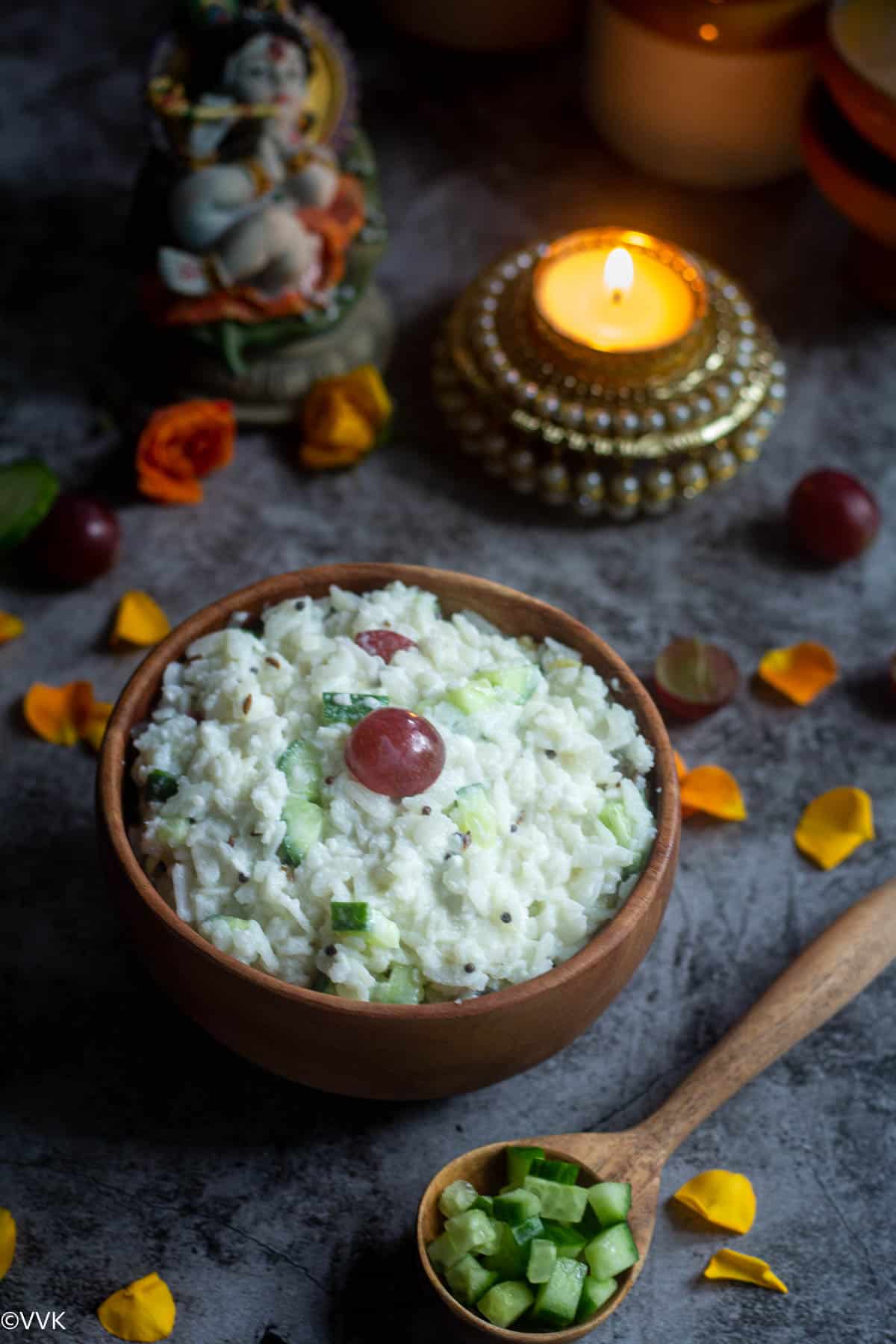 dahi poha served in wooden bowl with flower petals on the side and idol Krishna and candle on the top