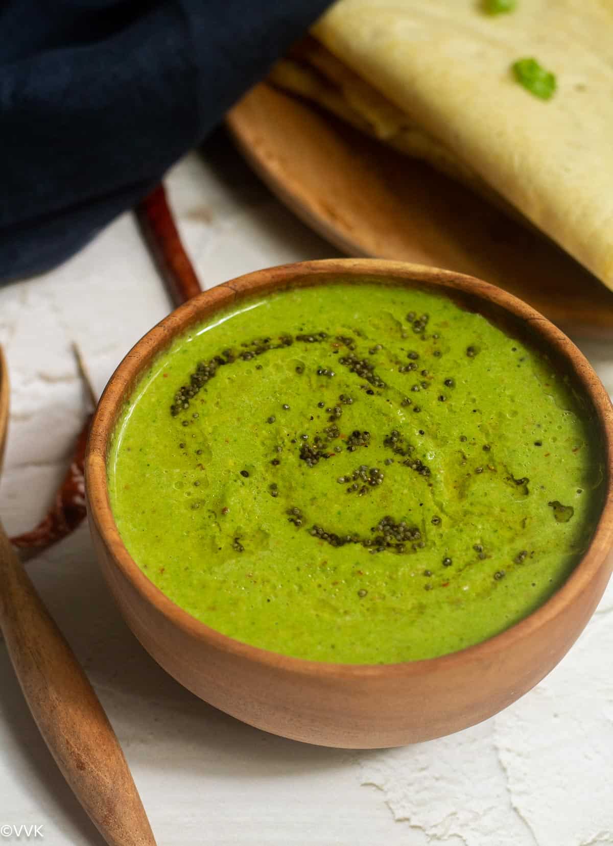 close up shot of coconut chutney served in wooden bowl with dosa on the top