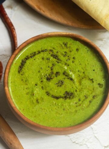 square image of coriander coconut chutney served with dosa in a wooden bowl and plate