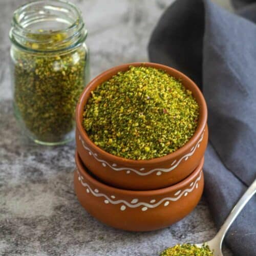 square image of cilantro podi served in terracotta bowl and in a bottle on the side