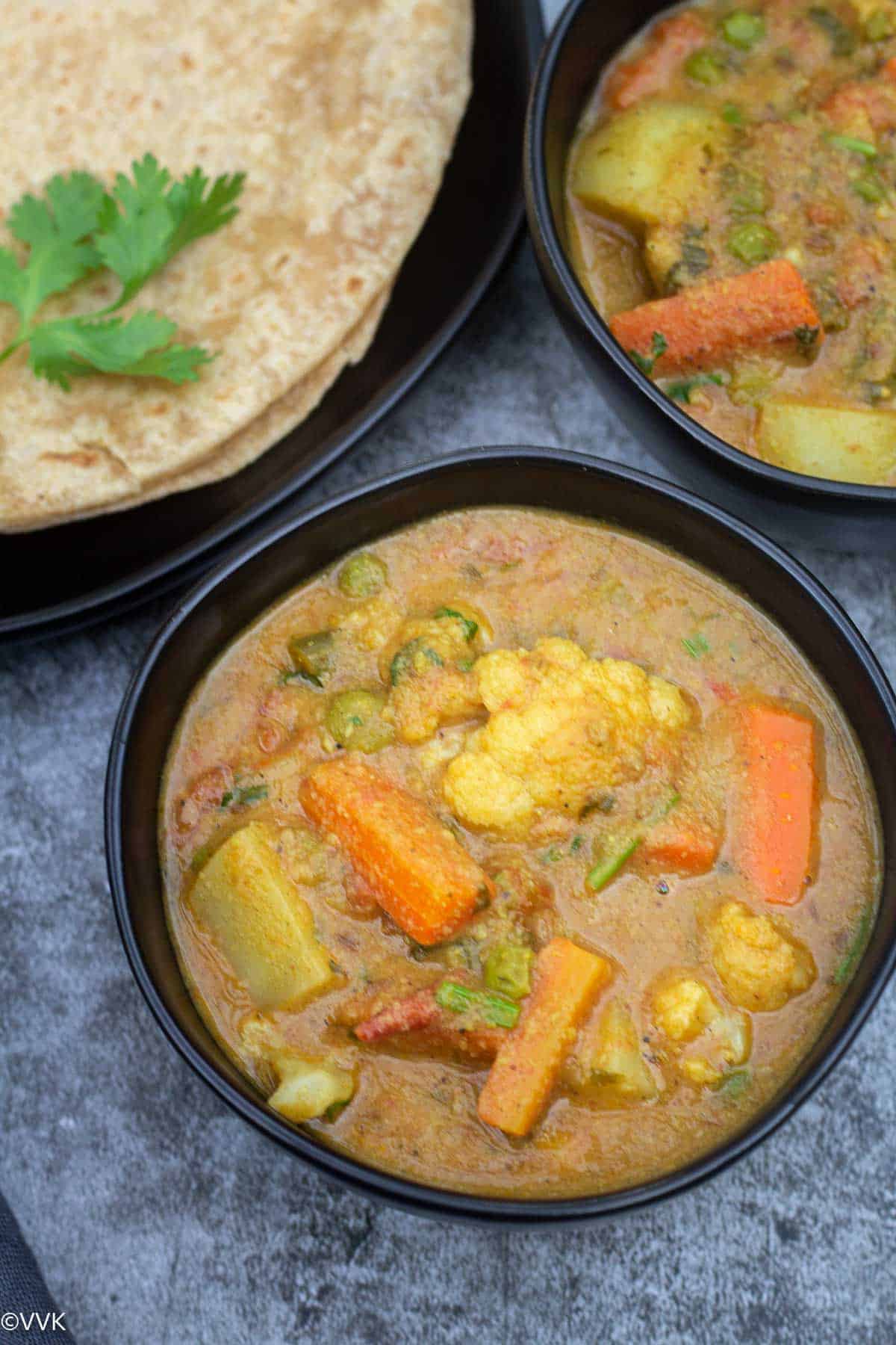 overhead shot of vegetable kurma served in black bowl with roti on the side