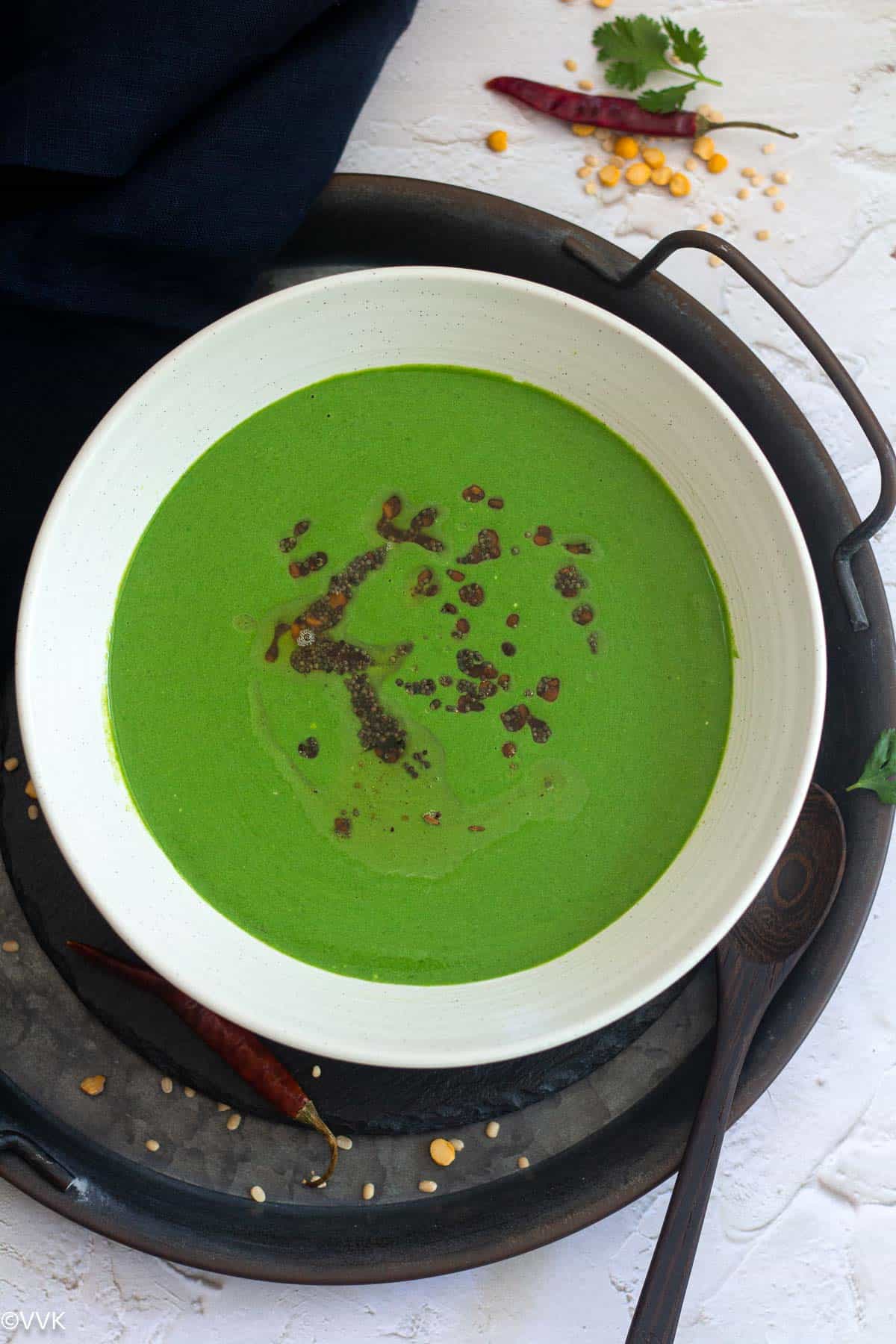 overhead shot of palak raita served in wooden bowl placed on black slate with a spoon on the side