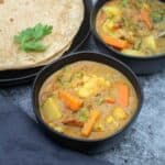 square image of veg kurma served in black bowl with roti on the side
