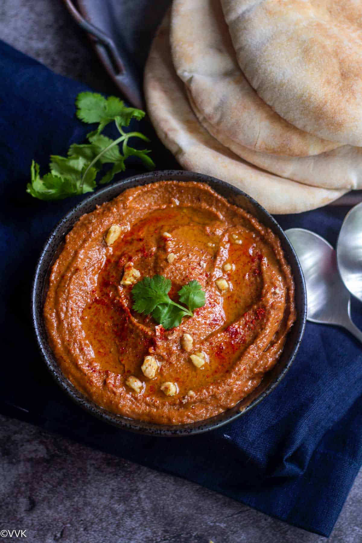 middle eastern  red bell pepper dip served in a bowl with pita bread on the side