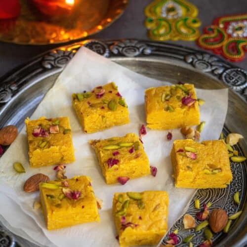 square image of milk barfi placed on silver tray with parchment paper