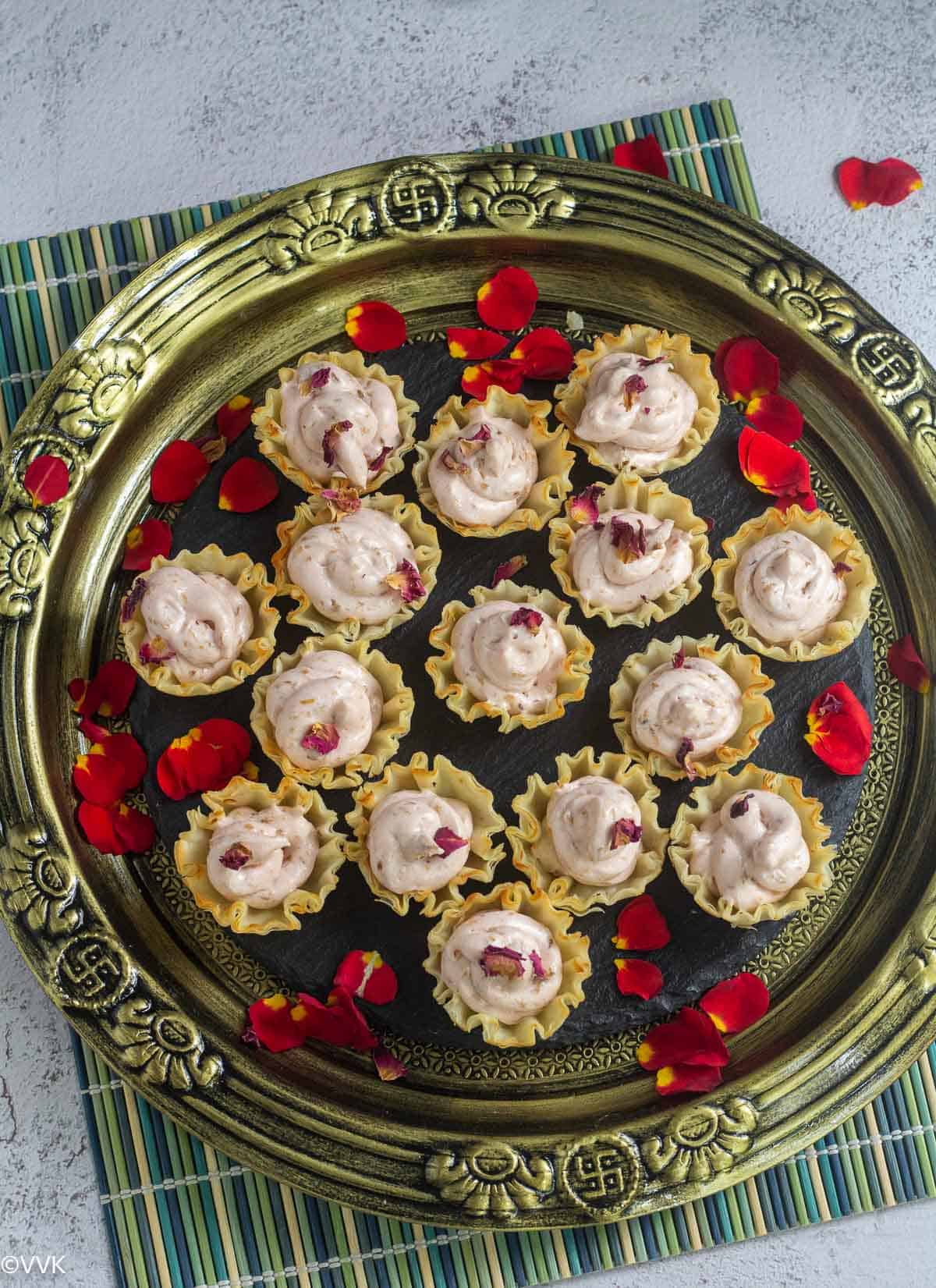 cream cheese dessert bites placed on golden plate sprinkled with rose petals placed on green mat