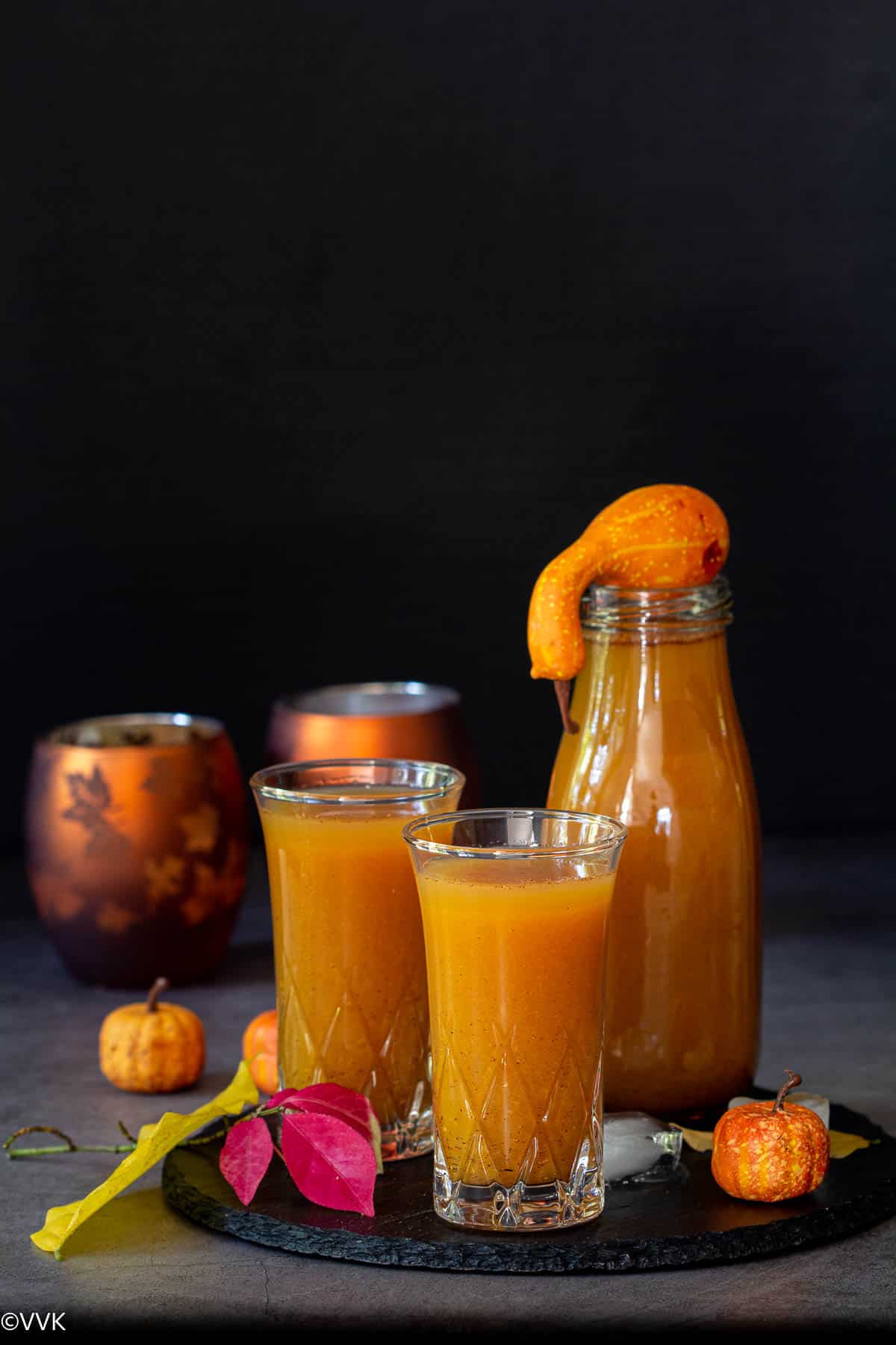 pumpkin juice served in two glasses and one bottle placed on top of black slate board