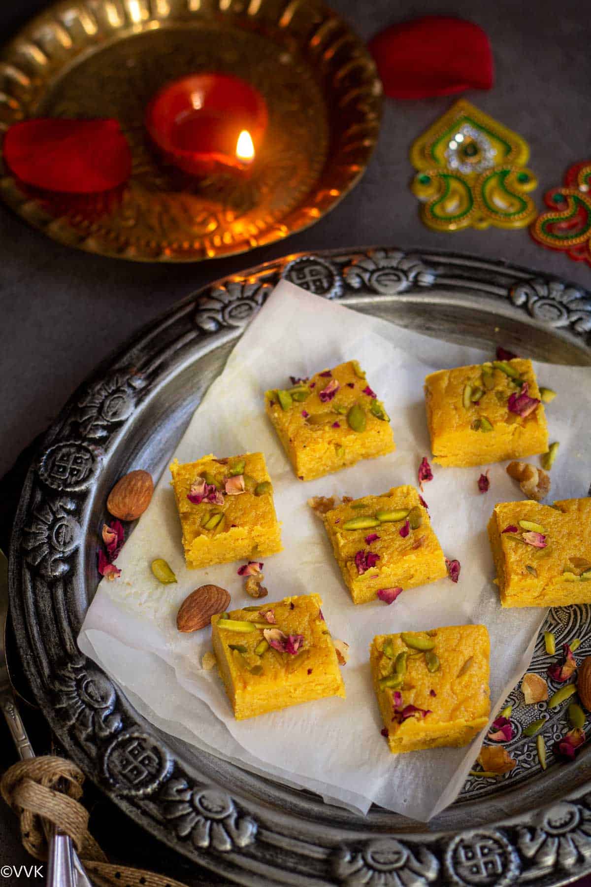 indian milk pudge with pumpkin puree placed on silver plate lined with parchment paper and a clay lamp on the side