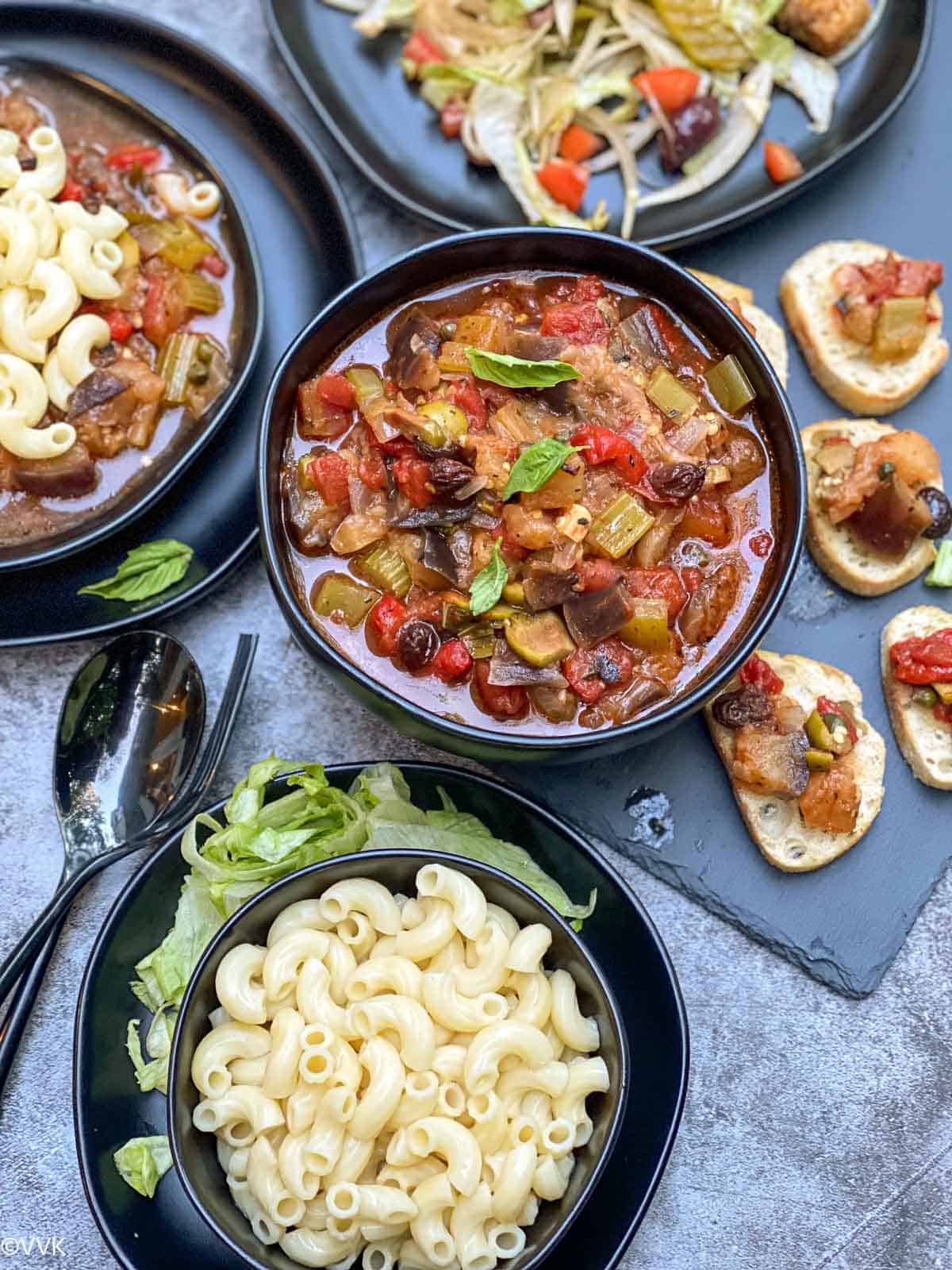 overhead shot of caponata with pasta, salad and brushetta