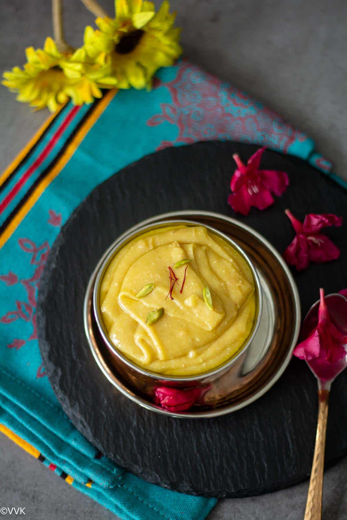 overhead shot of thirupagam served in bowl placed on black slate with flowers on the side