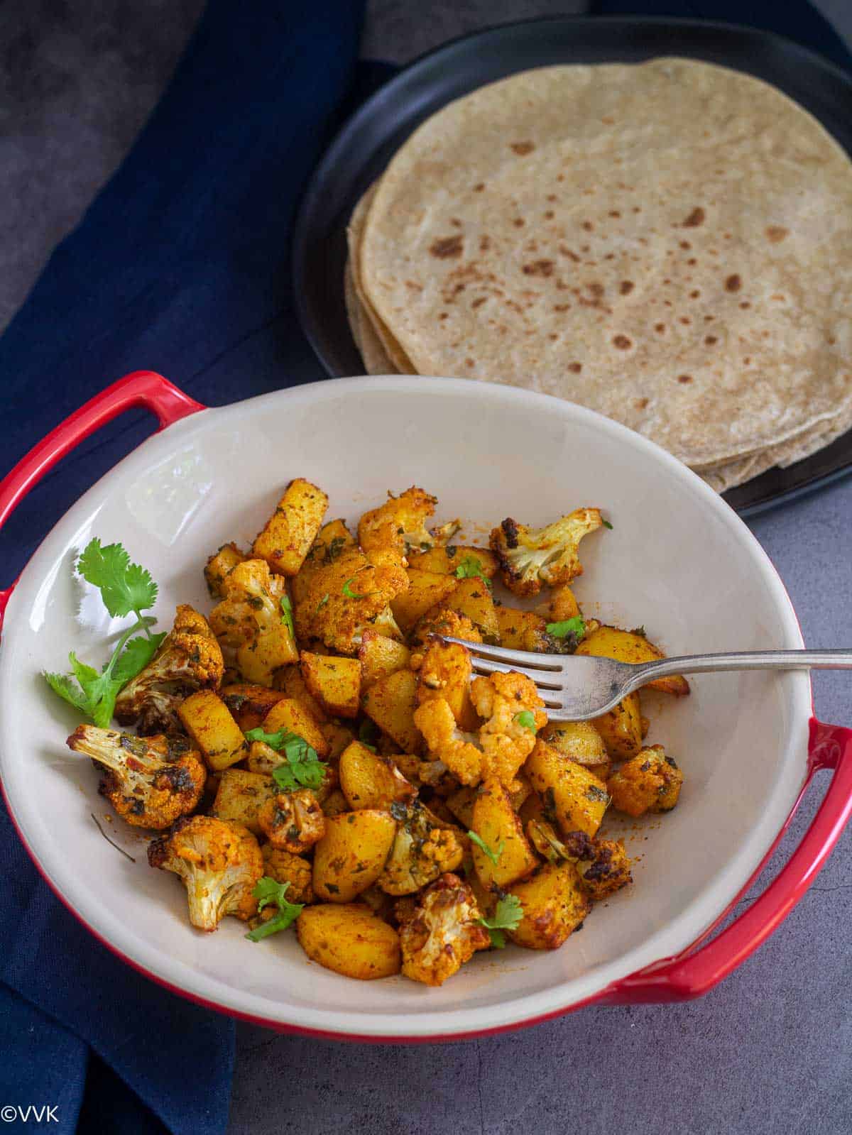 roasted potatoes and cauliflower with a fork inside served with roti