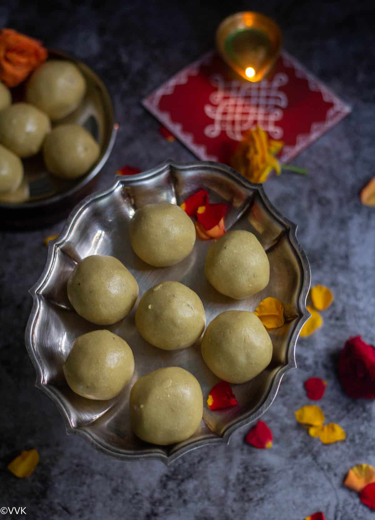 overhead shot of maladu placed in silver tray with a diya placed on kolam board behind