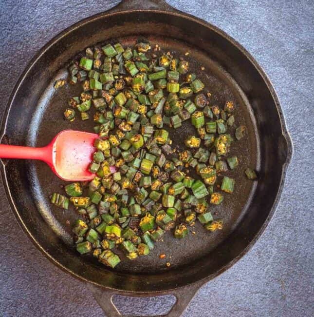 okra fry in cast iron pan with a red spatula