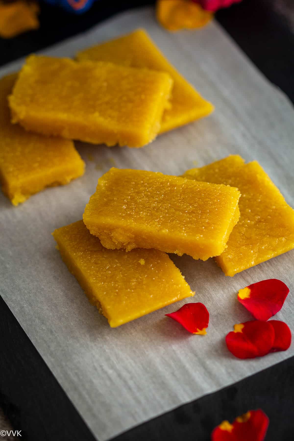 close up shot of mysore pak stacked up with rose petals on the side