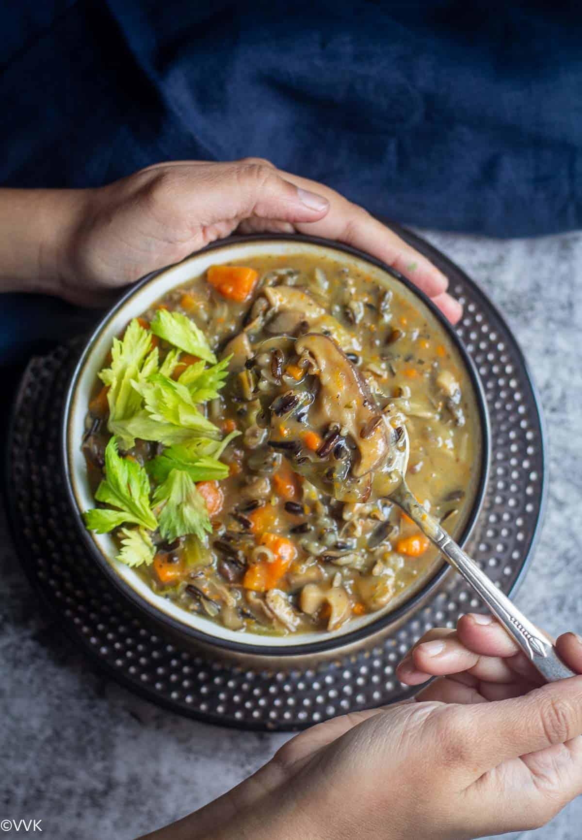 handheld shot of wild rice and mushroom soup with spoon inside topped with celery greens