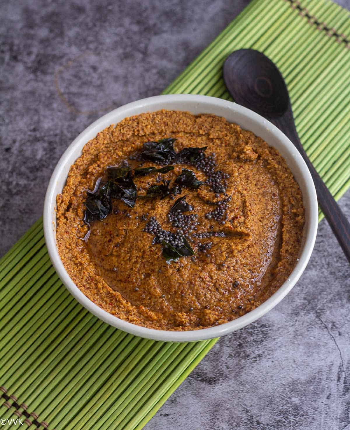 kanam chutney served in white bowl with a wooden spoon on the side placed on green mat