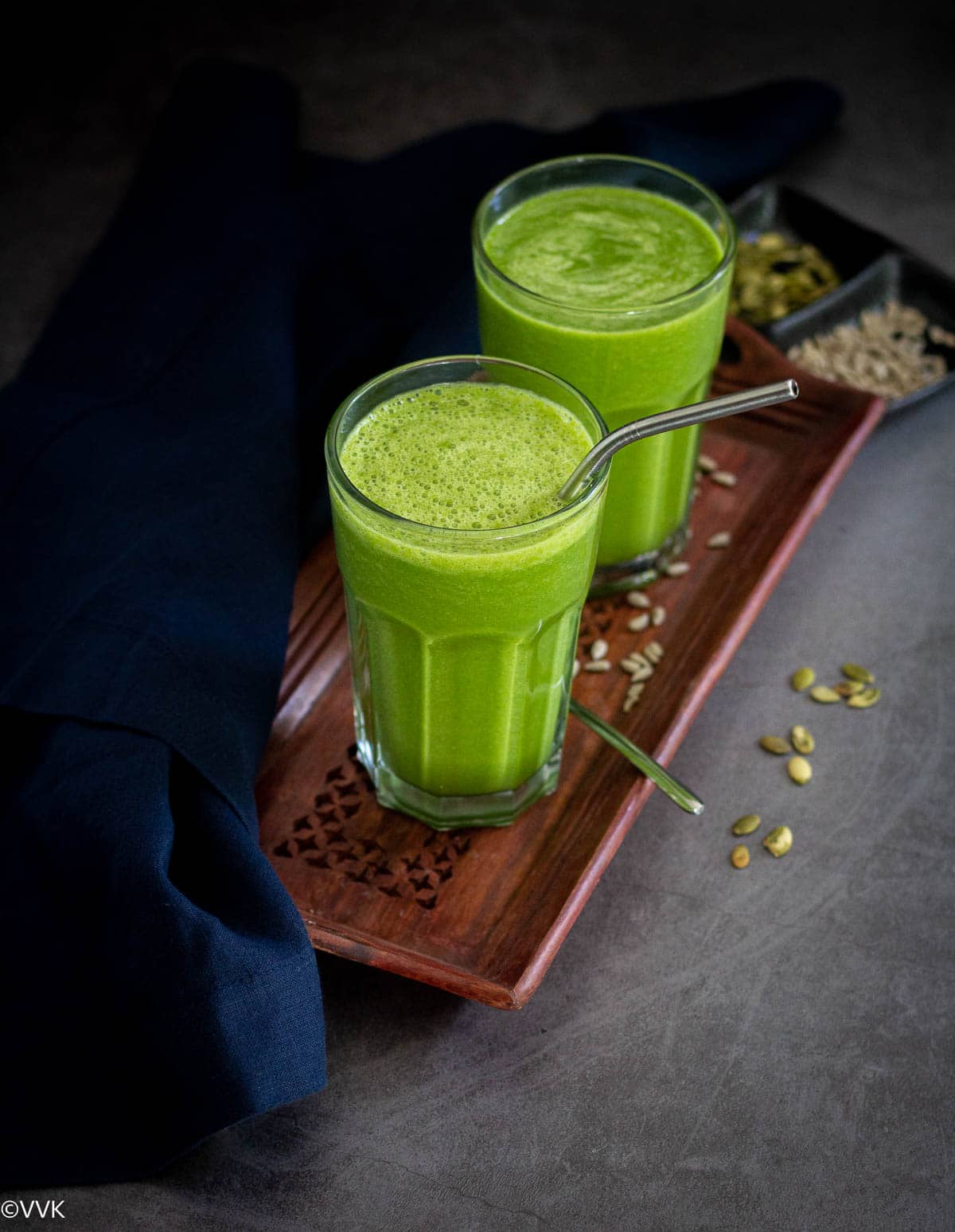 breakfast green smoothie in two glasses served on a wooden tray with seeds sprinkled