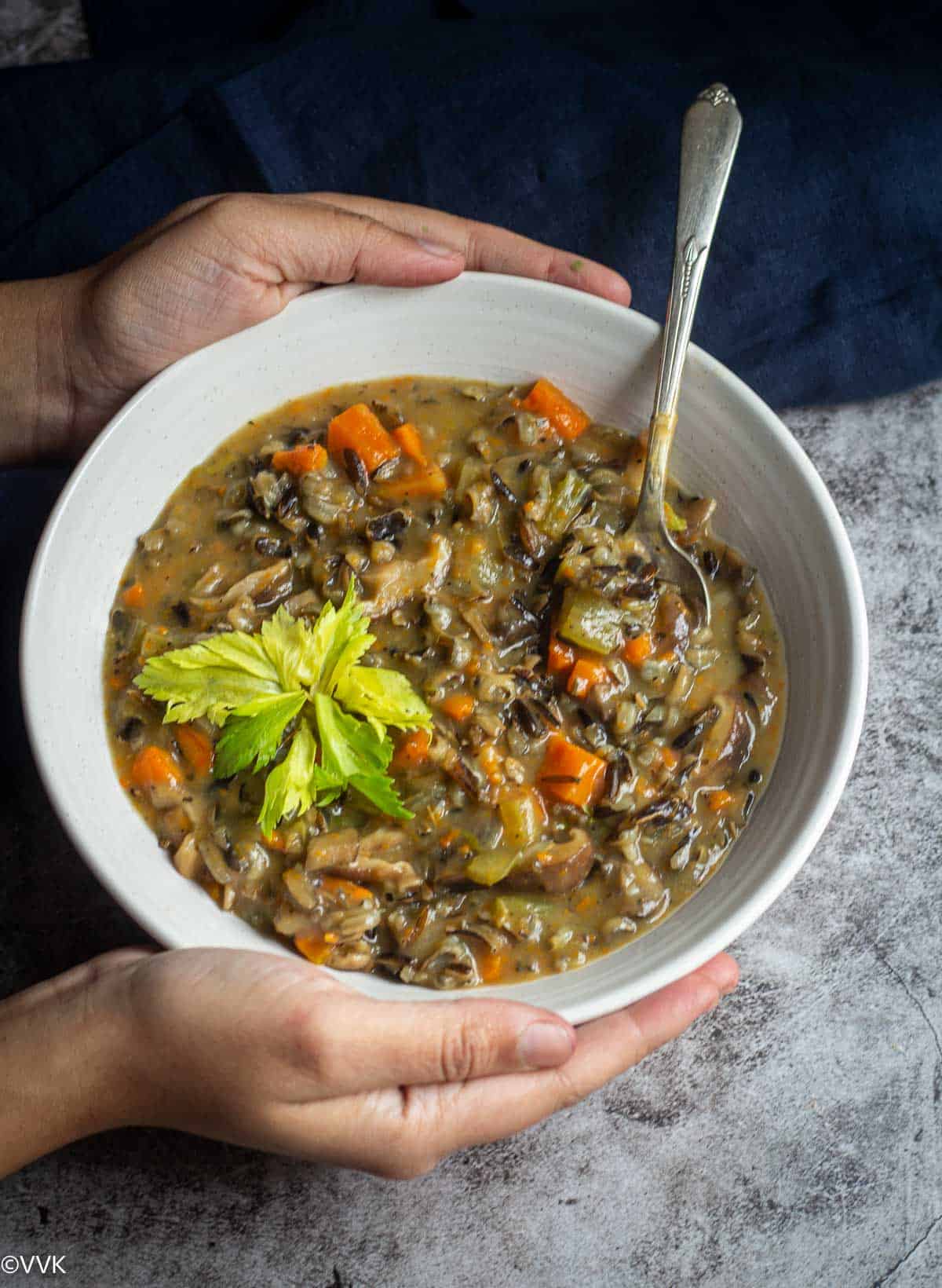 wild rice soup in white ceramic bowl with a spoon inside topped with celery greens