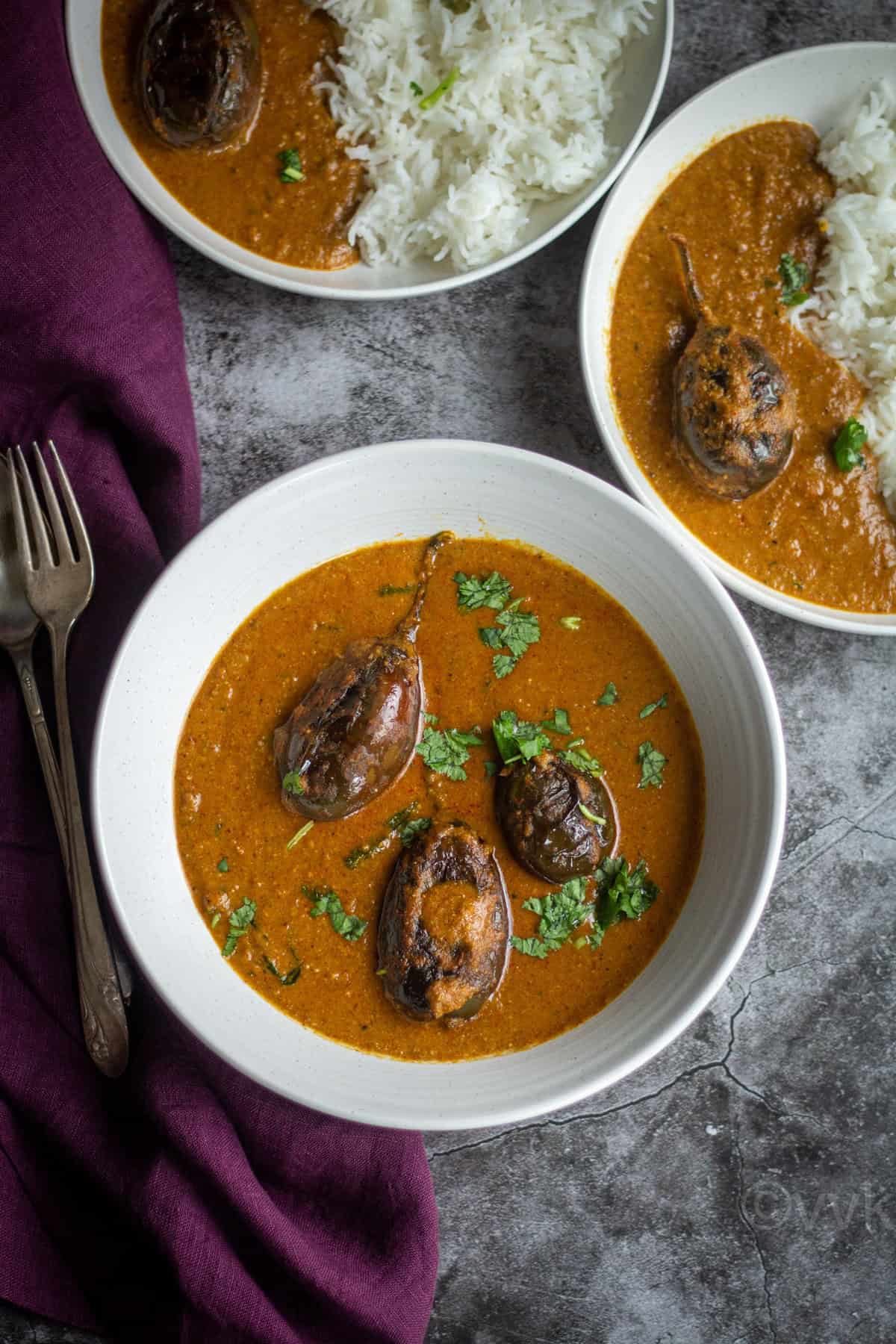 bagara baingan served in white bowl with some rice and same curry on the side in a different bowl