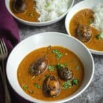 bagara baingan served in white bowl with curry and rice on the side