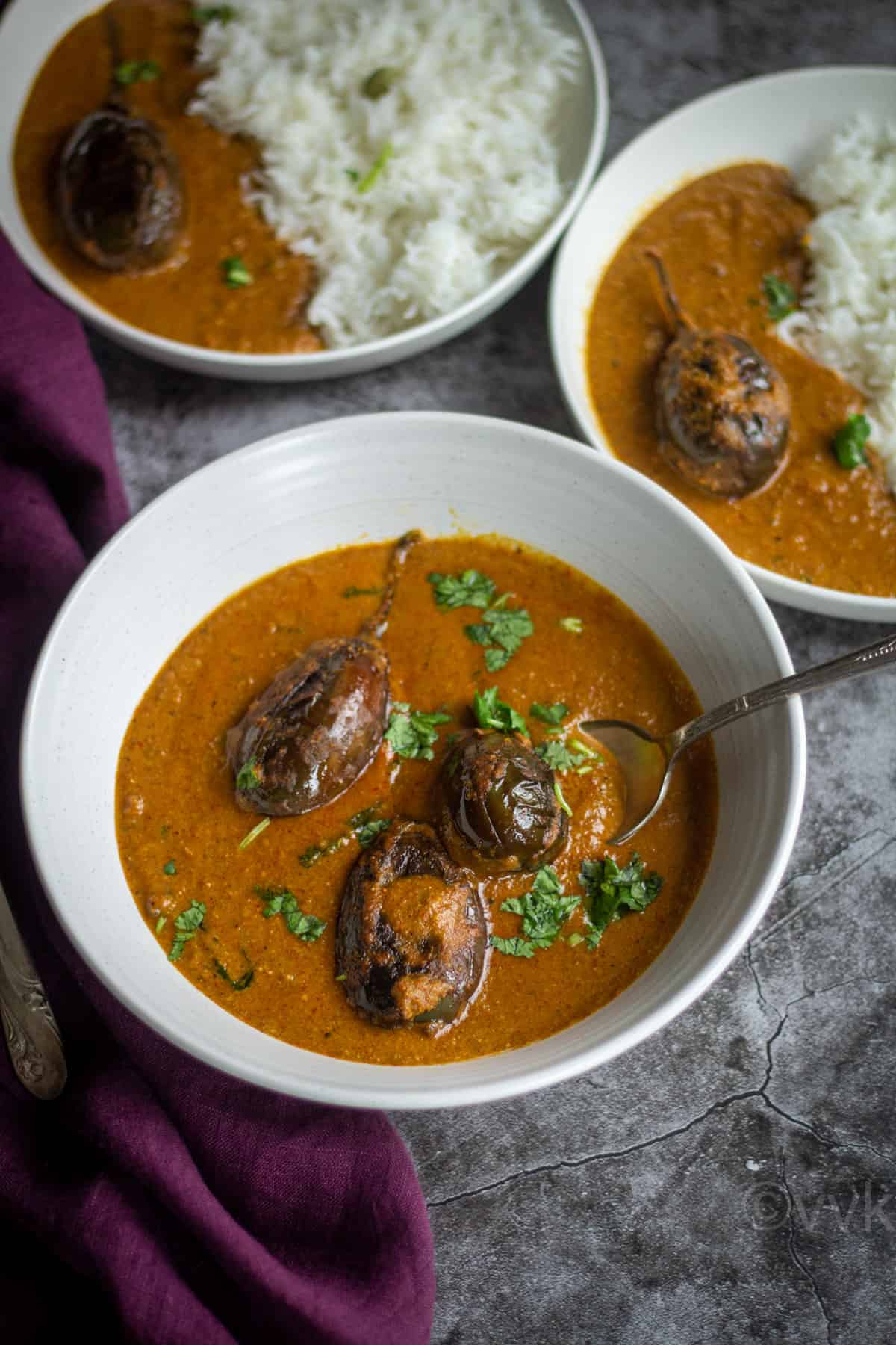 south indian eggplant curry in a white bowl with spoon inside