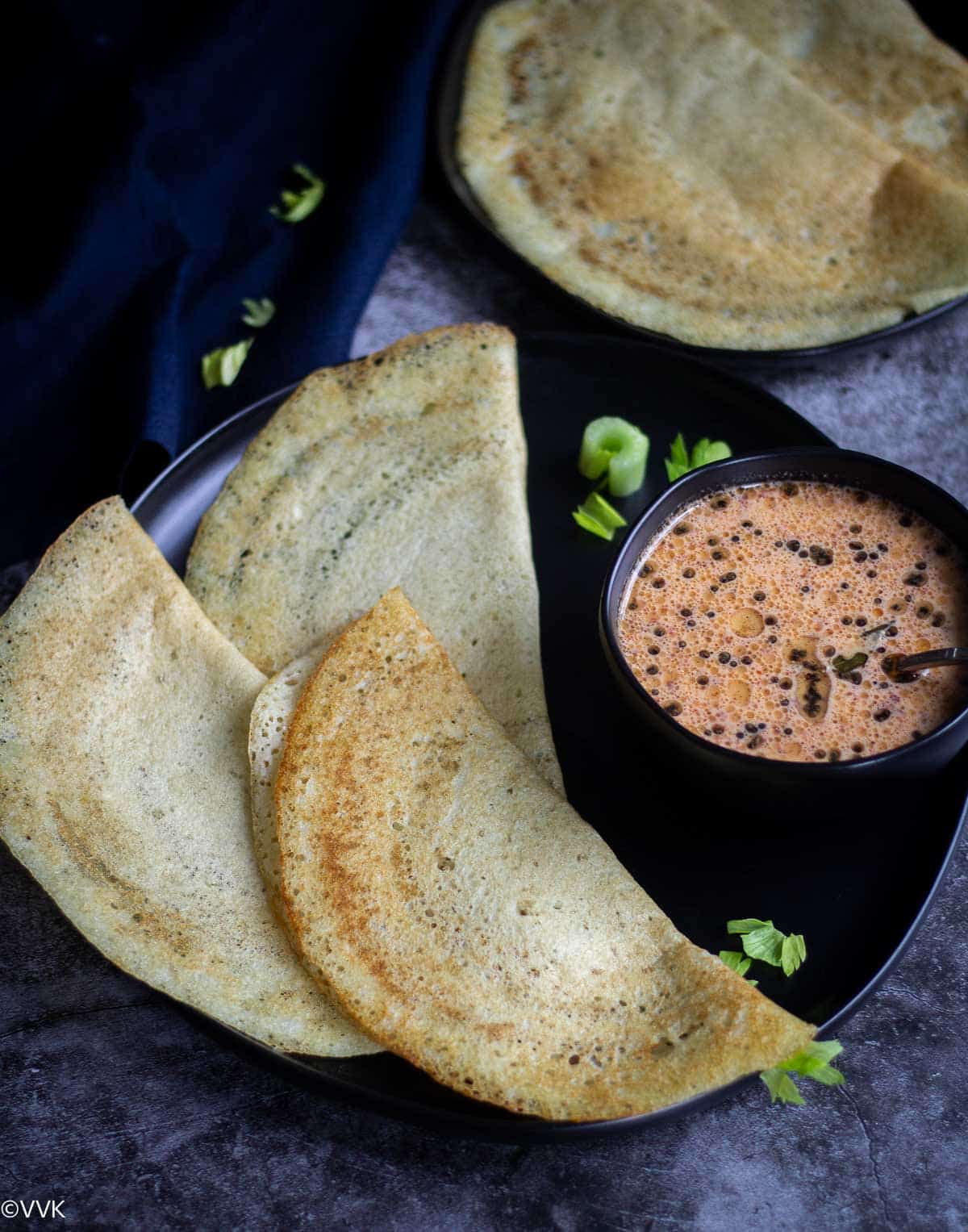 folded celery dosa served in black plate with chutney in black plate and bowl