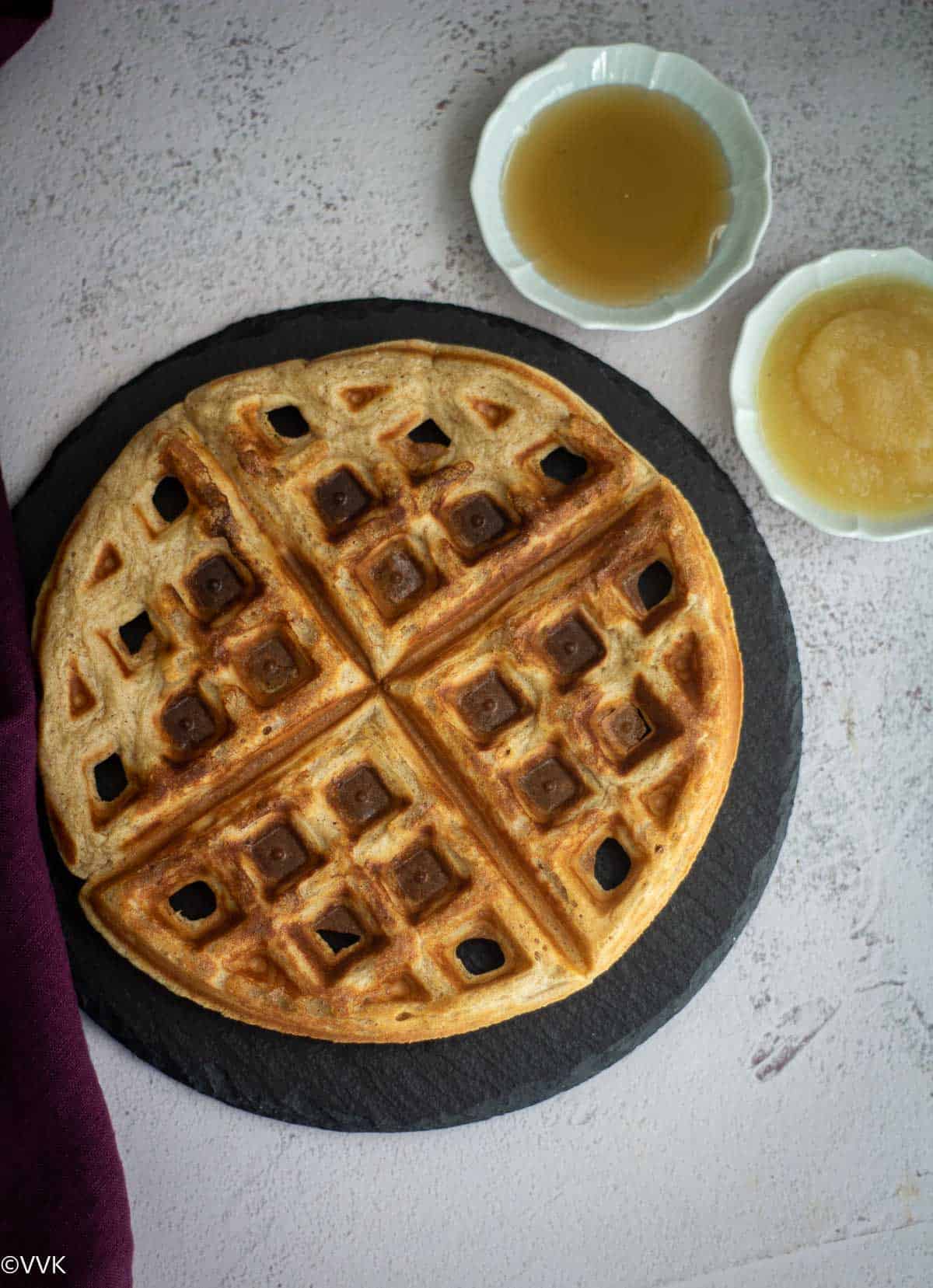 overhead shot of eggless applesauce waffles placed on slate board with applesauce and syrup on the side