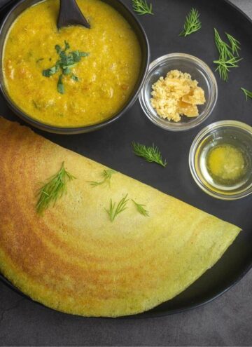 dill dosa served with kurma, jaggery and ghee placed on a black plate
