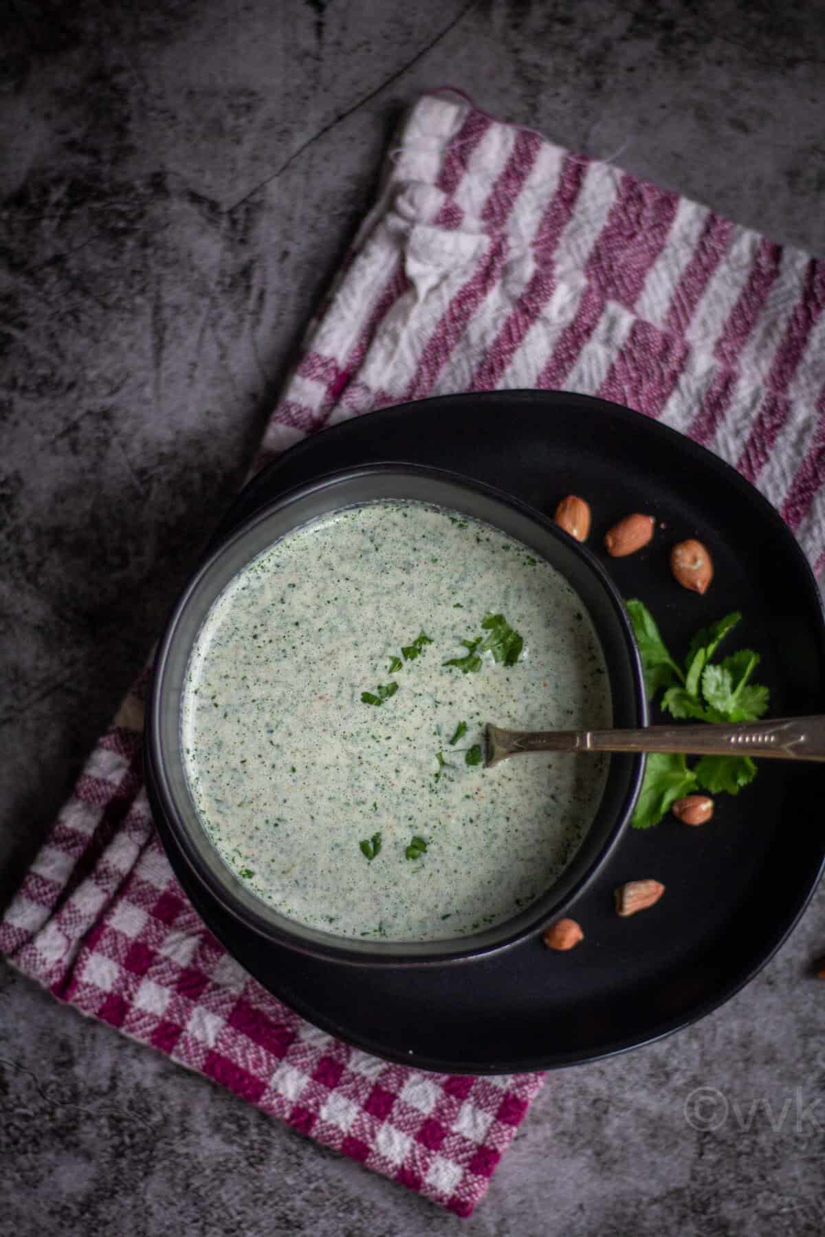 overhead shot of farali chutney served in black bowl with a spoon with peanuts on the side