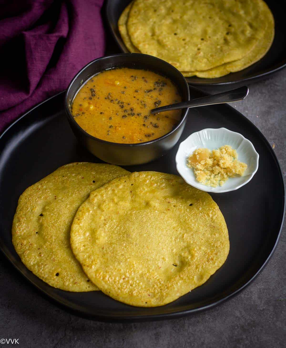 spicy edamame dosa served with sambar and jaggery served in black plate with more dosa on the side