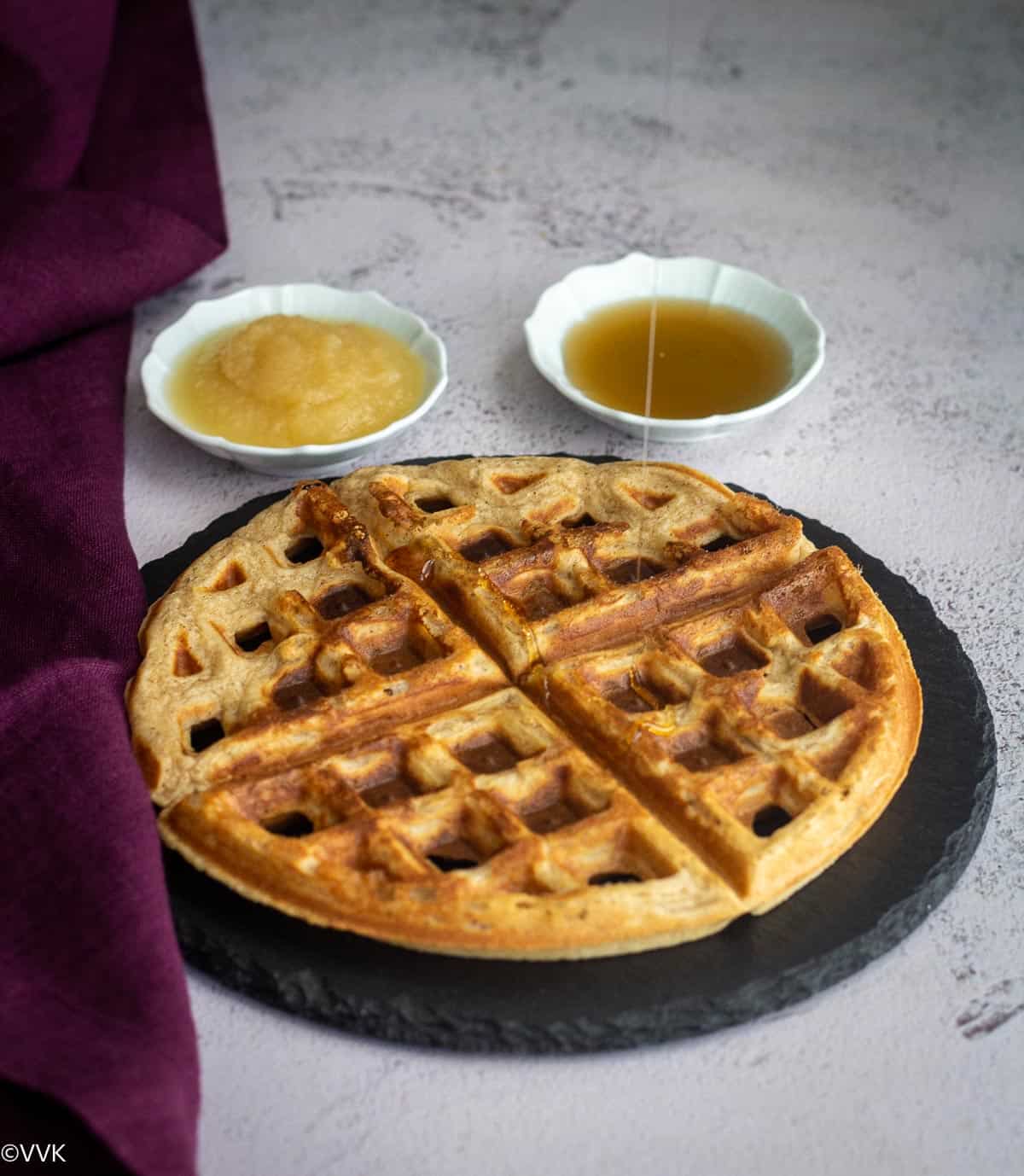 eggless waffles placed on slate board with a side of apple sauce and syrup