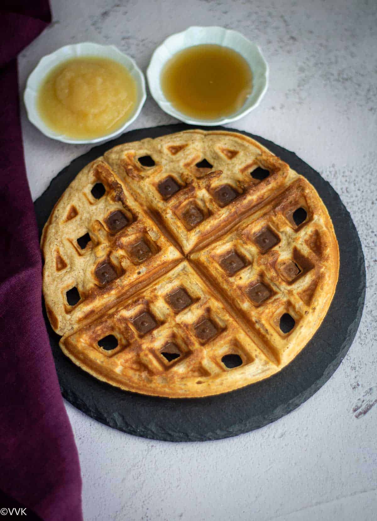apple sauce waffles served on black board with sides of apple sauce and syrup on the side