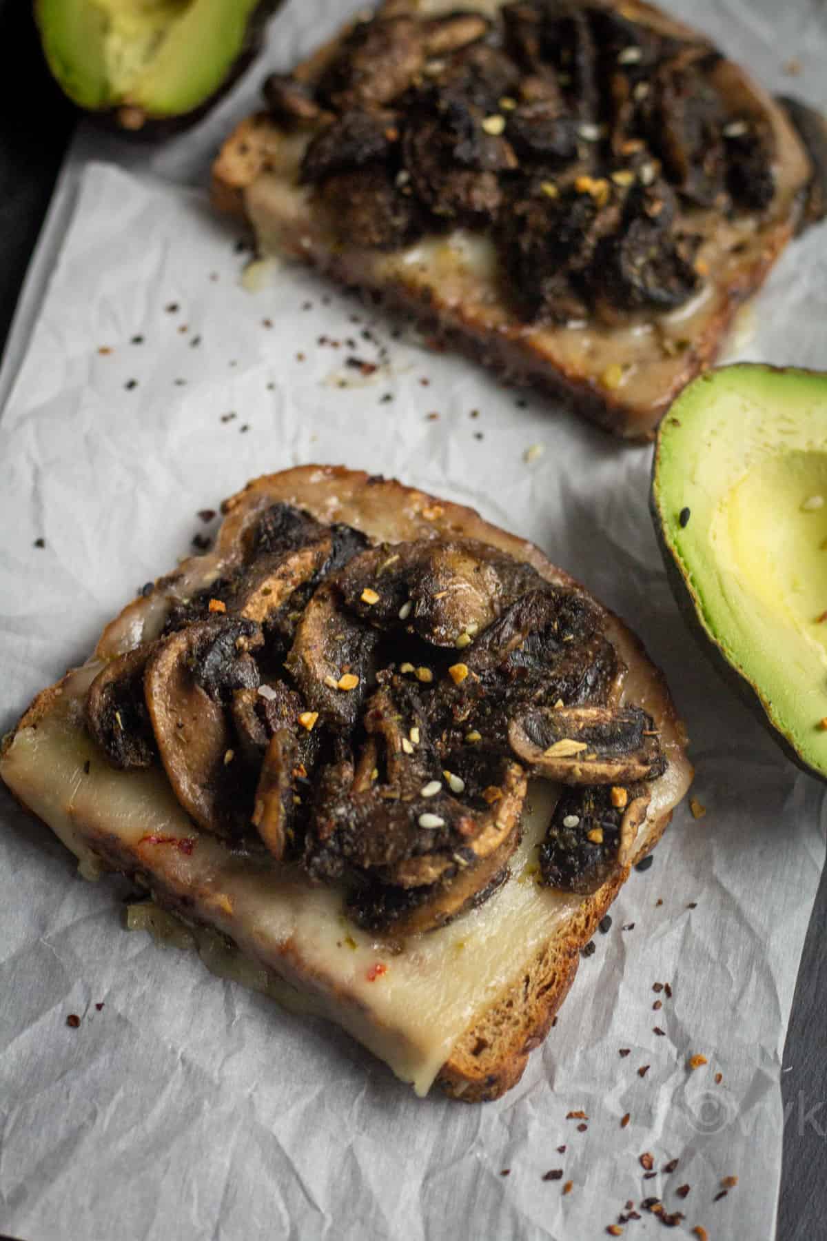 close up shot of the toast placed on parchment paper with avocado on the side