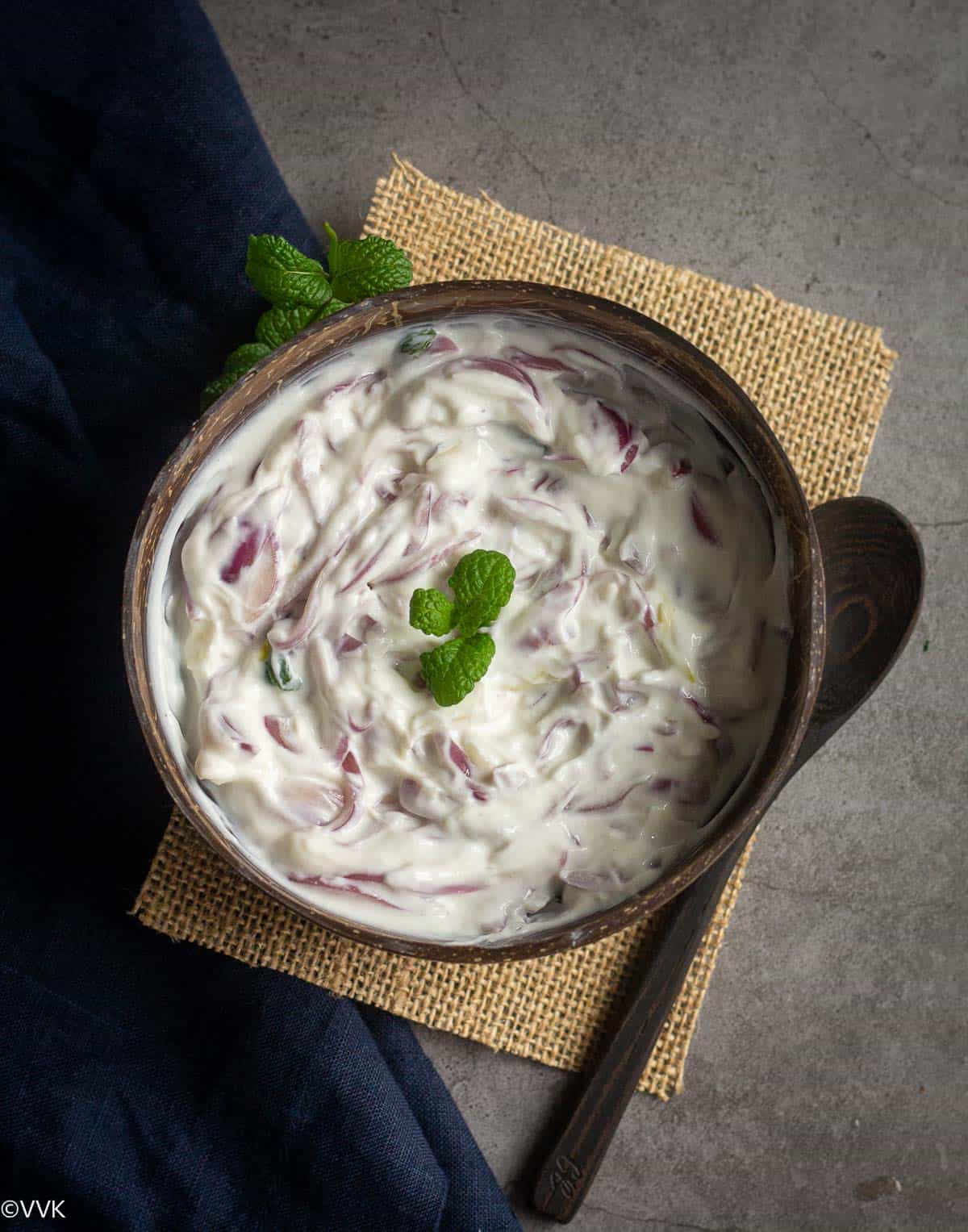 creamy onion raita recipe for biryani and pulao served in coconut bowl with spoon on the side