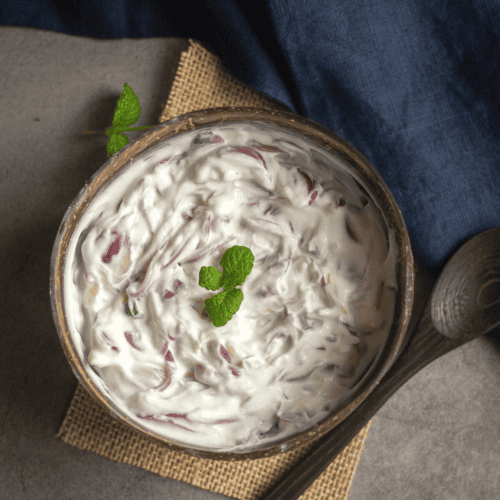 onion raita served in coconut bowl placed on burlap cloth