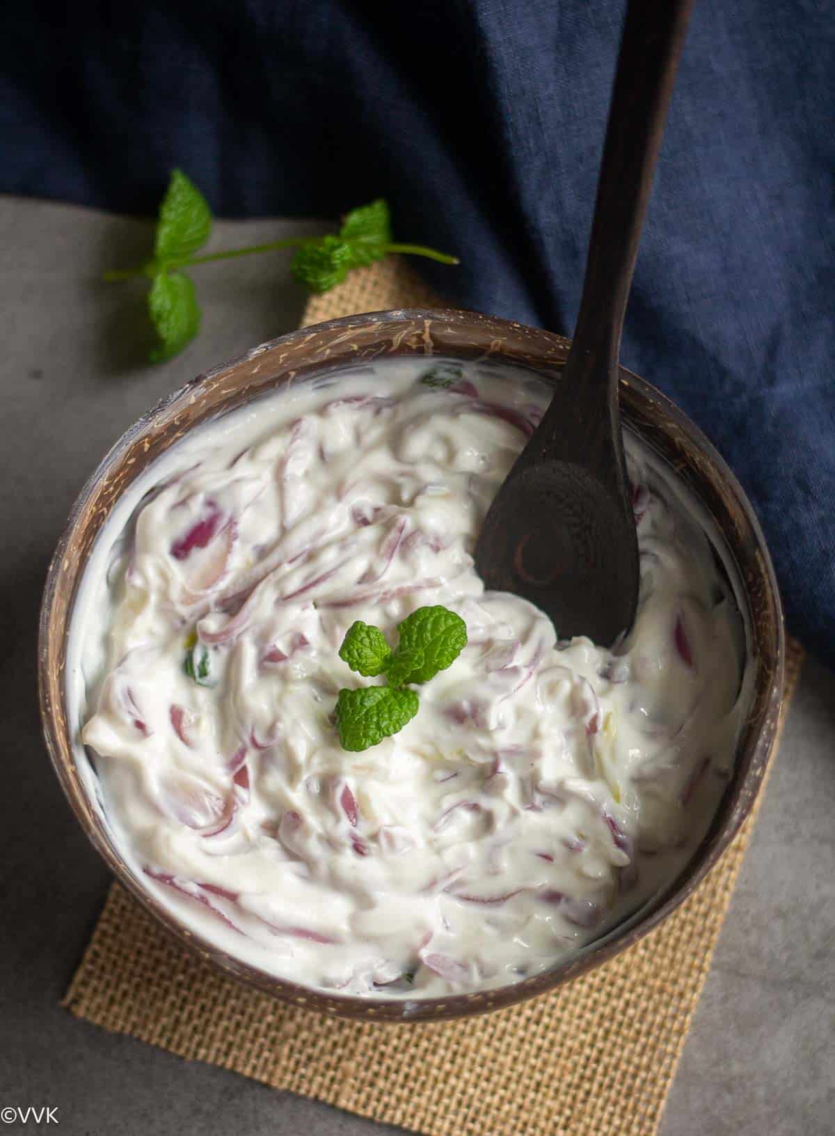 pyaz ka raita served in coconut bowl with spoon inside placed on burlap cloth