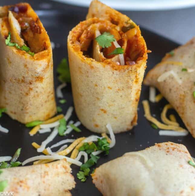 single jini dosa roll served in black plate with cheese drizzled