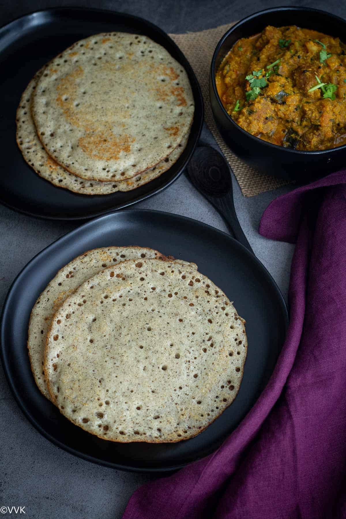 over head shot of kal dosai served in black plates with vada curry on the side