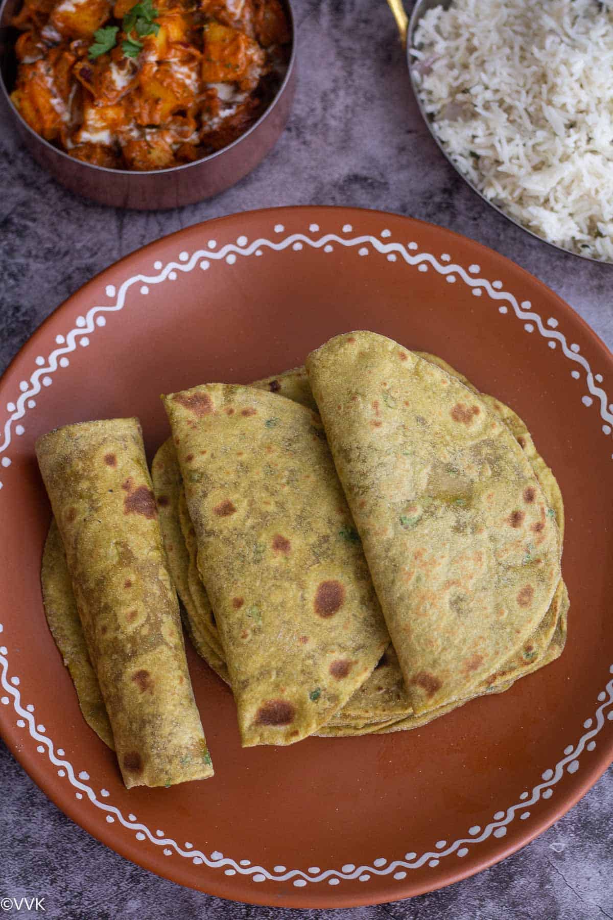 avocado chapati folded and placed on a terracotta plate with rice and curry on the side