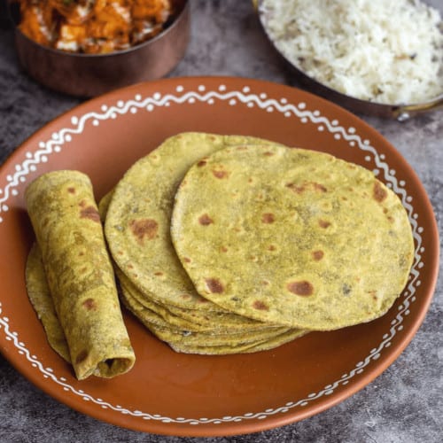 stack of avocado chapati and one rolled chapati placed on a terracotta plate
