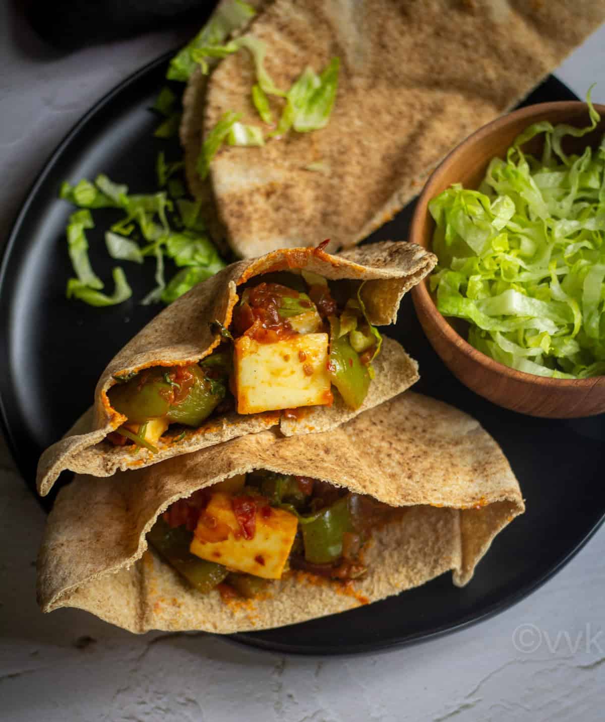 stacked paneer pita pockets served in black plate with extra pita and bowl of lettuce