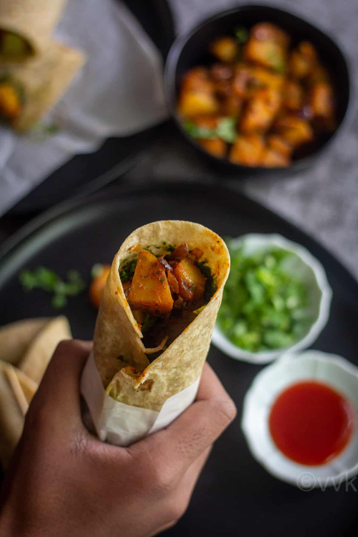 hand holding shot of roti roll and a plate below with cilantro and ketchup