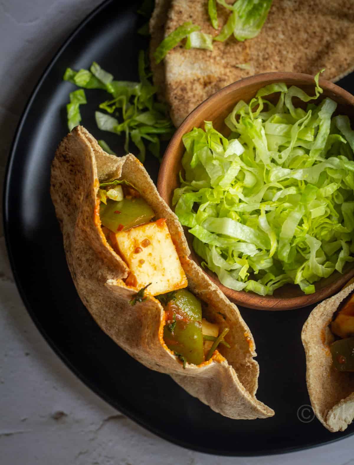 close up shot of single pita pocket filled with schezwan paneer with a bowl of lettuce on the side