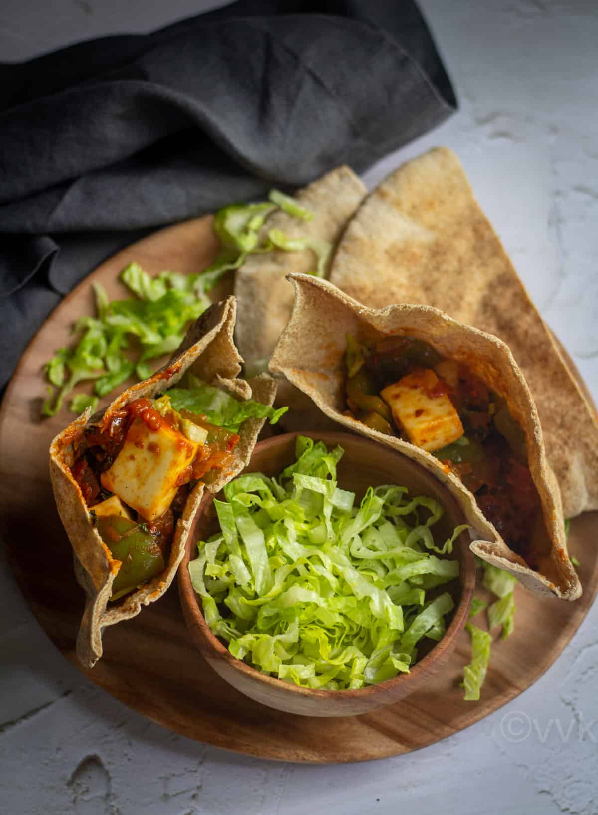 two pita pockets filled paneer placed on wooden plate with chopped lettuce on the side