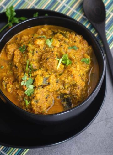 vada curry gravy served on black bowl placed on a green mat