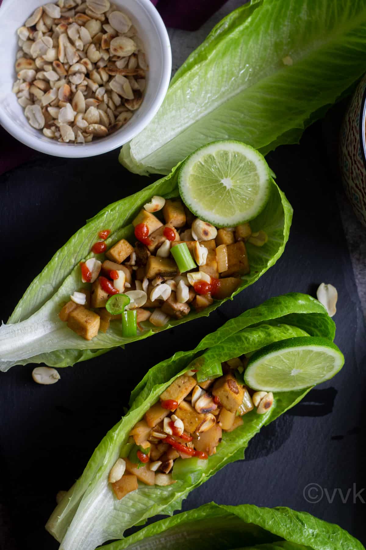 close up shot of veggie lettuce wraps served on a black slate board with peanuts on the side