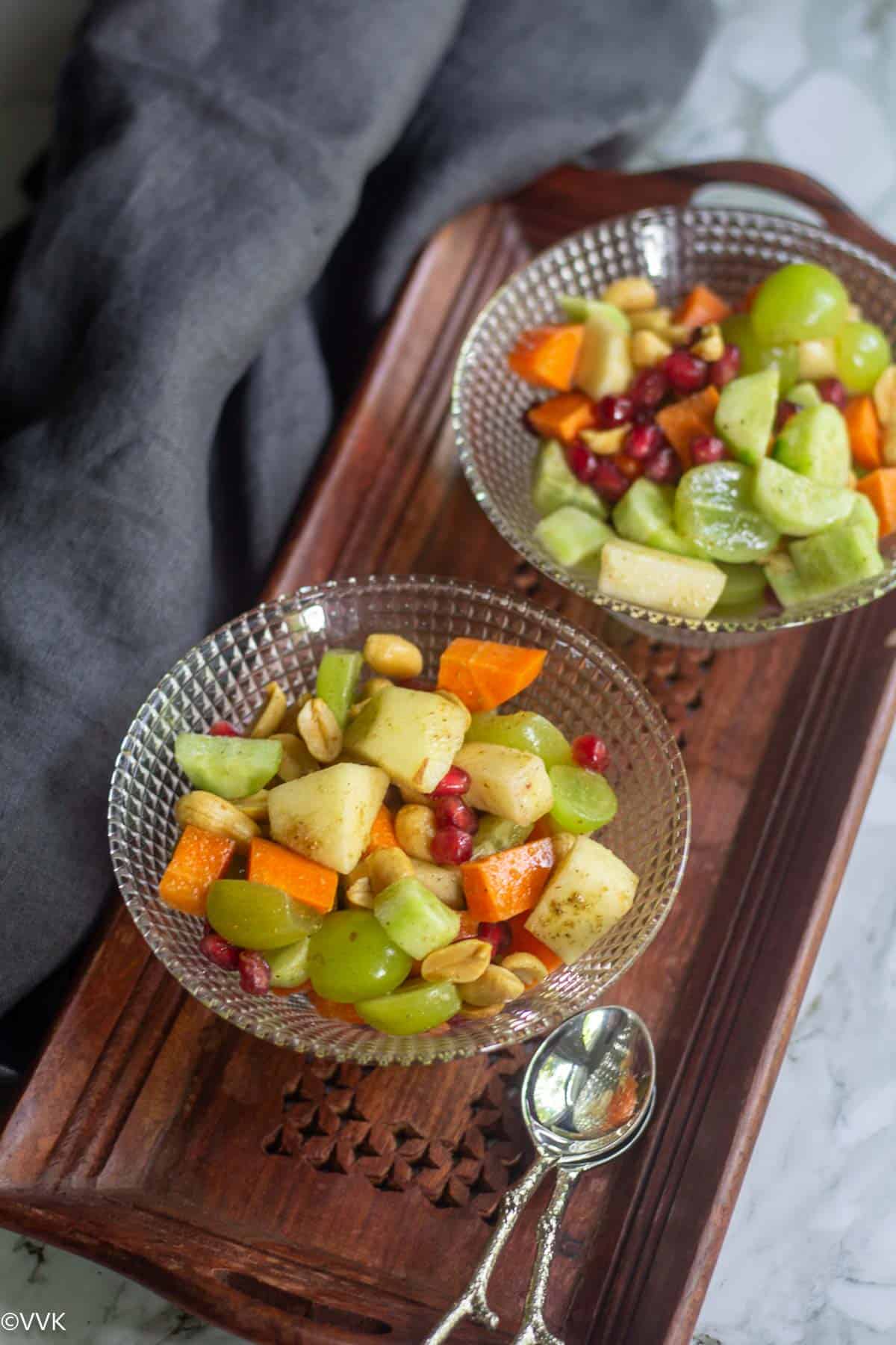 slanting shot of fruit and vegetable salad served in glass bowls placed on wooden board