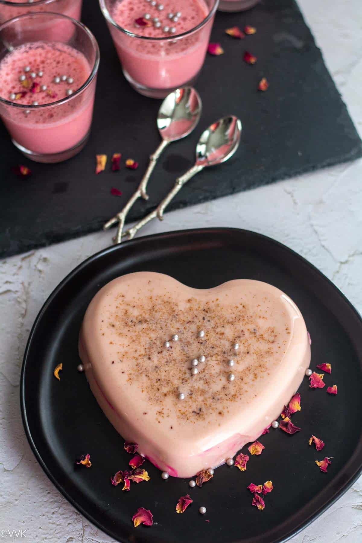 heart shaped panna cotta placed on black plate with rose petals drizzled