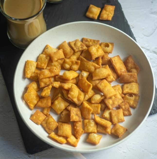 square image of namak para served in white bowl with coffee on the side