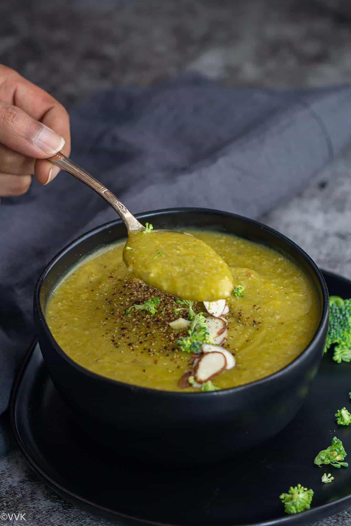 close up hand held shot of broccoli soup in a black bowl with gray fabric on the side